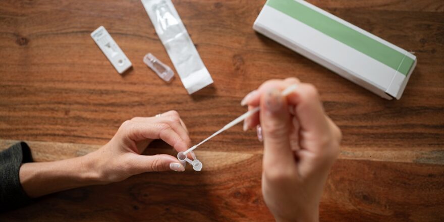 Top view of a woman dipping a swab stick of coronavirus self testing kit into a solution.