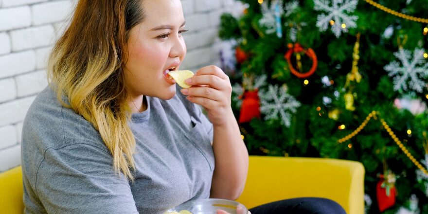 Fat girl is eating potatoes chips and watching TV in her house during Christmas time with concept relaxation at home during Christmas holiday.