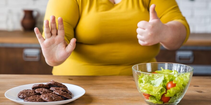 Pensive fat chubby obese caucasian woman opting for healthy food instead of sweets. Dieting concept. Hard choice between healthy lifestyle and bad eating habits.